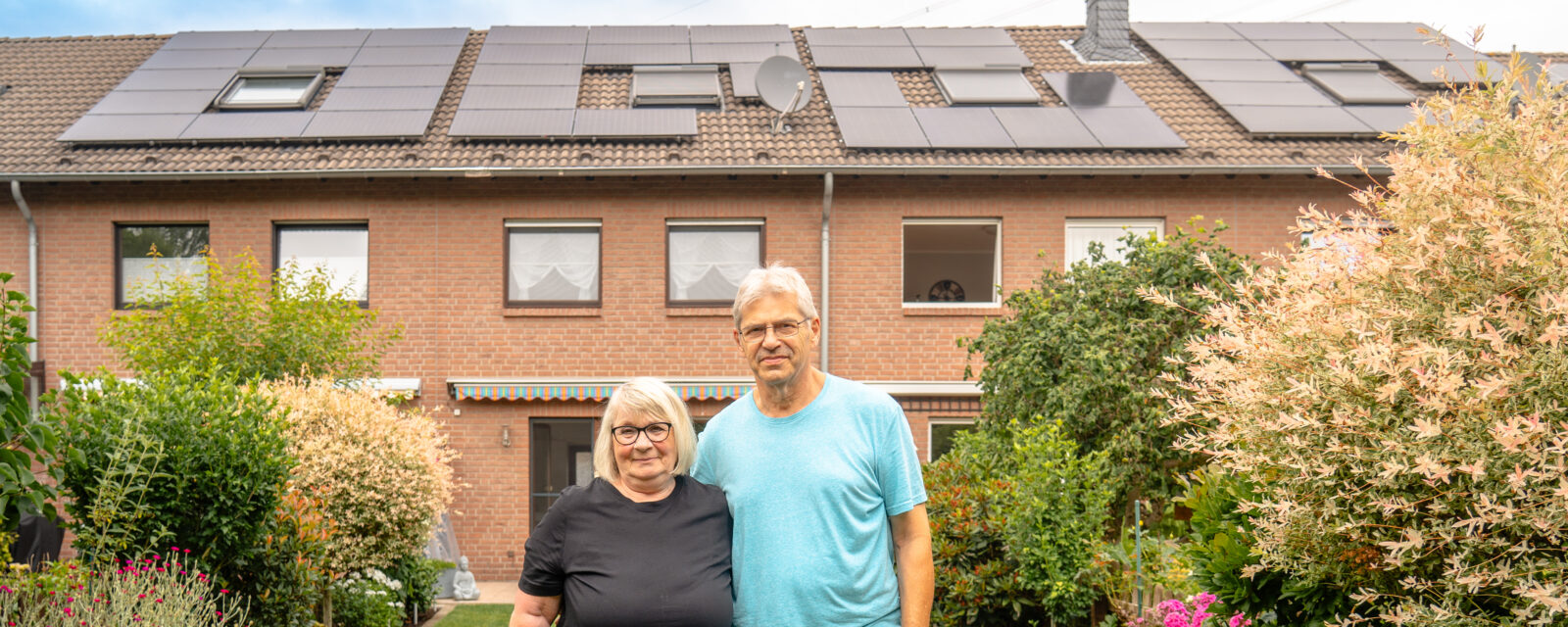 Glückliche evoyo Kunden im Garten vor ihrer Solaranlage bei Sonnenschein.